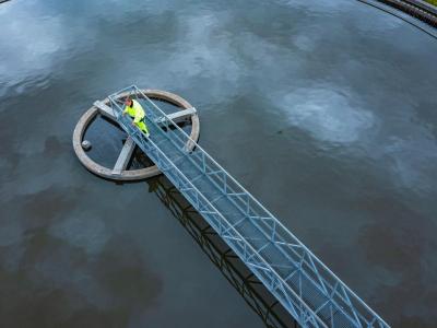 Mand i gult står på bro over et rensebassin